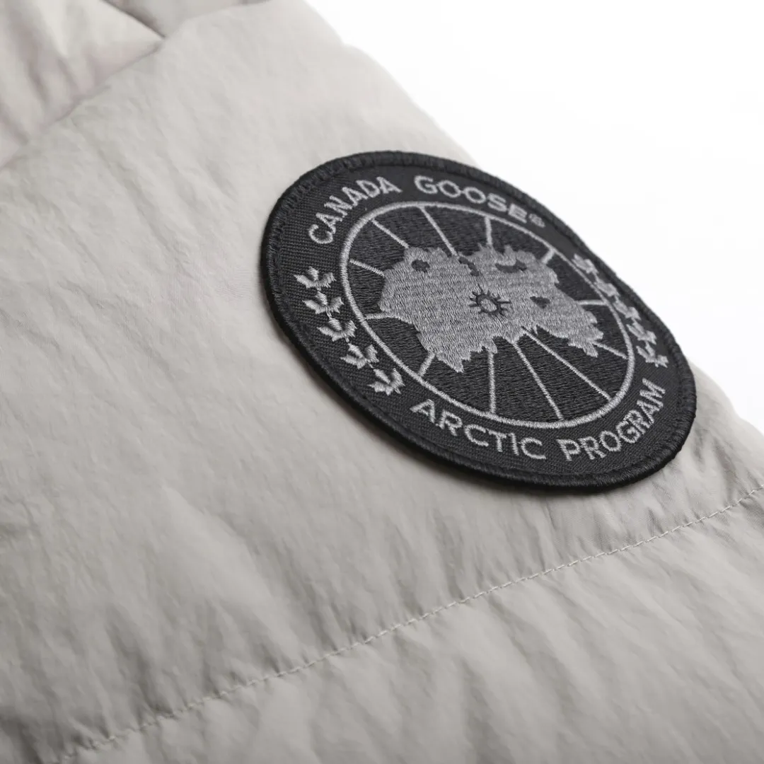 P980 Canada Goose hooded down jacket Fabric selection: Weaved with 400T high-count yarn. After special water-repellent treatment, the surface forms a lotus leaf effect - raindrops will slide down in beads, and snow particles will fall off when touched. The tear resistance reaches 200N (approximately 20kg load-bearing), the light gray matte texture breaks the stereotype of "outdoor clothing = hardcore", and the soft luster presents a high-end matte effect under urban neon lights, seamlessly switching scenes from ski resorts to CBD office buildings.  Process 1: Use polyester woven ribbons as the base, and use high-precision computer embroidery to decorate the brand letters on the ribbons. The edges of the pattern are clear, the stitches are fine and even, and multiple layers of embroidery threads are stacked to enhance the three-dimensional effect.  Process 2: Precision thread reinforcement to prevent velvet drilling and ensure that the fluffy and resilient elasticity lasts as new.  Details: The embedded cuffs are three-dimensionally woven to form a "wavy" elastic structure, forming natural folds when fitting the wrist, increasing the contact area with the skin, thus improving the windproof effect. At the same time, micro-velvet treatment is added to the inside of the cuffs, which feels like a second layer of skin and avoids friction on the skin from metal zippers or hard fabrics.  90 national standard high-quality white duck down: selected high-loft down, weighing 240g, light and warm, with excellent temperature locking performance and good resilience.  Accessories: 1:1 customized armband, 1:1 customized zipper pendant, 1:1 customized elastic buckle, etc. SIZE: S M L XL